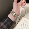Detailopname van elegant goud ovaal horloge met kristallen ring en grijze leren band - Numerieke schaal / Cijfers-Grijze Band Witte Wijzerplaat