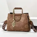 Detail van bruine leren tas met gouden kettinghandvat en parelhanger in bladvorm - Karamelbruin (Stijl 1)