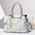 Close-up of elegant embroidery textures and gold leaf pendant on a white floral handbag - Light Gray