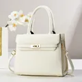 Detailed view of white lychee leather texture and golden metal twist lock on tote bag - 28cm x 11cm x 22cm / White