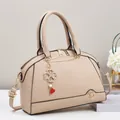 Dettaglio borsa beige con texture grana litchi e ciondolo a cuore quadrifoglio - Cachi