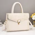 Detail view of beige crocodile embossed leather bag with elegant golden ring lock - White