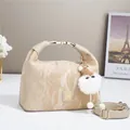 Elegant beige textured handbag with plush charm and gold hardware on white surface - Khaki