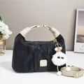 Black pleated tote bag with plush charm and beige handles in a minimalist setting - Black
