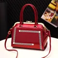 Red patent leather handbag with pearl details and Greek Key pattern on white desk - Burgundy