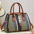 Détail du sac cabas jacquard rayé avec sangles en cuir et boucle dorée sur un mur beige - Vert Militaire