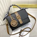 Fashionable black pebble leather handbag with silk scarf handle and smiley face pendant - Black