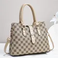 Detailed view of beige checkered tote bag with brown leather handles and gold lock closure - Plaid Khaki