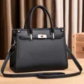 Classic black litchi pattern leather handbag with gold metal lock on wooden table - Black