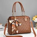Detail der braunen Handtasche mit Logo-Muster, goldenen Ketten und dekorativem Seidenschal - Erdgelb