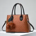 Brown ostrich pattern tote bag with plush cherry charm on a white display stand - Earthy Yellow