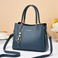 Detail of dark blue leather handbag with gold logo, heart charm and pearl accessory - Blue