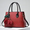Macro shot of red ostrich texture handbag with cherry plush charm and golden metal hardware - Wine Red