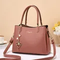 Detalle del bolso de piel rosa con herrajes dorados, colgante de corazón y grabado - Rosa