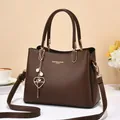 Detail of brown leather handbag with gold lettering, pearl heart charm and strap - Coffee