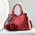 Donkerrode lederen handtas met kersenhanger op een witte minimalistische sokkel - Rood