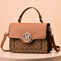 Detail der karamellbraunen Handtasche mit M-Monogrammmuster und goldenem Metalllogo - Erdgelb