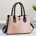 Detail of pink crocodile embossed leather tote bag with black handles and metal buckles - Pink