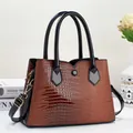 Detail of brown crocodile pattern handbag with black faux leather straps and metal hardware - Khaki/Earth Yellow