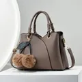 Brown lychee leather tote bag with cherry pom-pom charm on a white pedestal display - Khaki