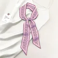 Dettaglio della sciarpa in seta viola con motivo paisley annodata su un abito di raso crema - Viola Paisley