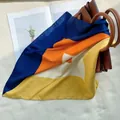 Detalle de un pañuelo de seda con bloques de color geométricos en un bolso de cuero - Naranja