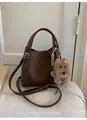 Close-up of brown litchi grain leather bucket bag with plush dog charm and silver hardware - With Pendant / Coffee