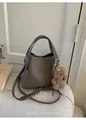Detail of dark khaki lychee leather bucket bag with cute brown bear charm on sofa - With Pendant / Gray