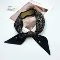 Close-up of a black silk twilly scarf with ethnic prints tied in a decorative bow knot - T392-1 Black Base Floral