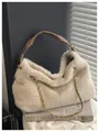 Plüschige cremefarbene Hobo-Tasche mit goldener Kette und braunem Griff auf Kunstbüchern - Aprikose
