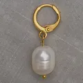 Elegante gouden oorbel met witte barokparel op getextureerde grijze stoffen achtergrond - Enkele Tonvormige Barokparel Stijl