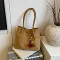 Brown matte tote bag with plush keychain charm resting on a book and suitcase - With Pendant / Yellow
