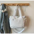 Detail of white nylon tote bag with multiple zippers and wide webbing handles hanging - White