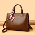 Detailansicht der dunkelbraunen Leder-Handtasche mit Seidenschal und Gold-Hardware - Kaffeebraun