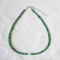 Détail d'un collier de perles vertes avec perle centrale sur tissu blanc texturé - Style A (Vert/Or)