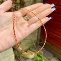 Close-up of 2-3mm orange natural stone beads on a dainty necklace held in hand - Orange Red Faceted Agate (I) / 38cm+5cm