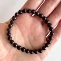 Detail van ronde dieppaarse granaatkralen op een elastische armband gehouden in de hand - Dieppaars Rood(Armband 32)