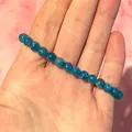 Detail van blauwe natuurlijke edelsteen kralenarmband vastgehouden in hand met licht - Blauwe Apatiet Stijl(Armband 38)