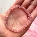 Detail van een roze natuurstenen kralenarmband in de handpalm op marmeren achtergrond - Rozenkwarts Stijl(Armband 40)