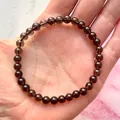 Detail van donkere edelsteenkralen op een elastische armband in de palm van de hand - Rookkwartskleur(Armband 42)