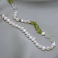 Gros plan d'un collier de perles baroques et pierres vertes sur du satin - Collier en titane avec pierres concassées vertes et perles d'eau douce