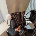 Bolso tipo cubo marrón oscuro con cordón, cadena dorada y colgante de pompón blanco - café