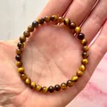 Hand met een goudbruine tijgeroog stenen kralen elastische armband voor dames - Goudbruin Tijgeroog(Armband 60)