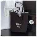 Detail view of black canvas tote bag with white merci text and striped strap accent - One Size / Black