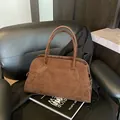 Chic dark brown frosted suede handbag with curved top and elegant strap on a magazine - Brown