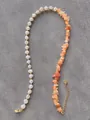 Detail van asymmetrische ketting met witte parels, oranje stenen en gouden accenten - Oranje Steen Parel Stijl