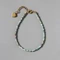 Macro shot of faceted green natural stone beads and gold heart pendant on a steel bracelet - Pale Green