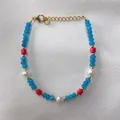 Detail van kralenarmband met blauwe stenen, rode accenten en witte parels op zijden stof - Blauwe Gefacetteerde Kralen Rode Accent Stijl (25SL1-3) / 17+3cm