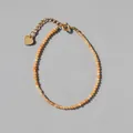 Macro shot of orange faceted beads and 18k gold heart charm on a delicate bracelet - Warm Orange