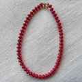 Detalle de collar de cuentas rojas con cierre de barra en T dorado sobre lino blanco - Collar I / Talla única / 43cm / Rojo